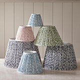Endon Caldgrove tapered lamp shades in pleated faux linen with leaf print, shown in pearl grey, blue, green and peachy tones against a panelled wall.