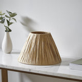 Caldwood 25cm tapered lamp shade in natural raffia with a woven texture, shown on a marble console table beside a vase and books.