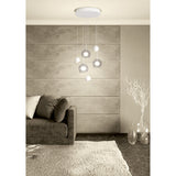Caprecano 6-Light Pendant in white, with round ceiling plate, white ball shades and clear glass globes at staggered heights, shown above a sofa in a living room.