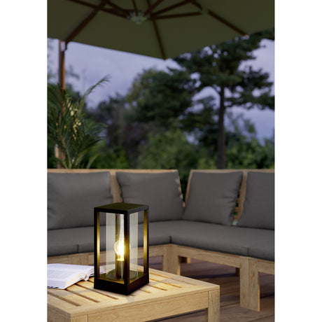 Cascinetta Outdoor Post Light in black, a square lantern-style fixture with cast aluminium frame and glass cylinder, shown lit on an outdoor patio table.