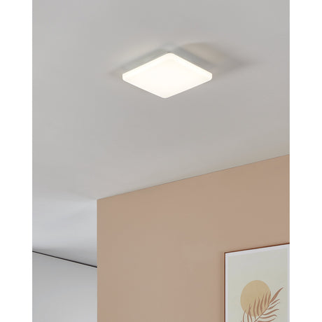 Castagneto LED Panel Light 26 x 26cm in white, a square ceiling fixture with rounded corners mounted flush on a white ceiling in a room with a pink accent wall.
