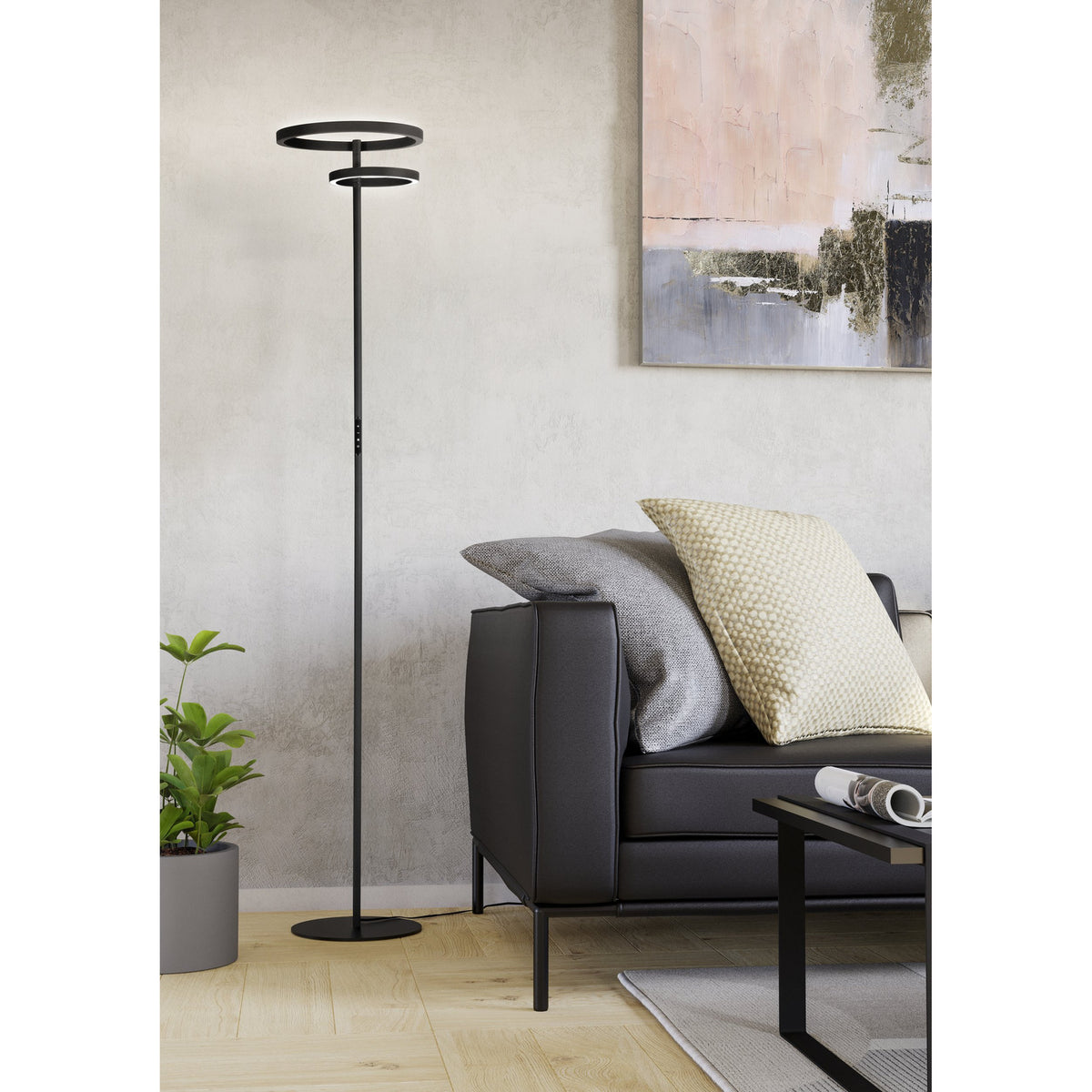 Castelpoto 1 LED floor lamp in black, tall slim pole with round base and two tiered open rings at the top, shown in a living room beside a dark sofa.