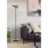 Castelpoto 1 LED floor lamp in black, tall slim pole with round base and two tiered open rings at the top, shown in a living room beside a dark sofa.