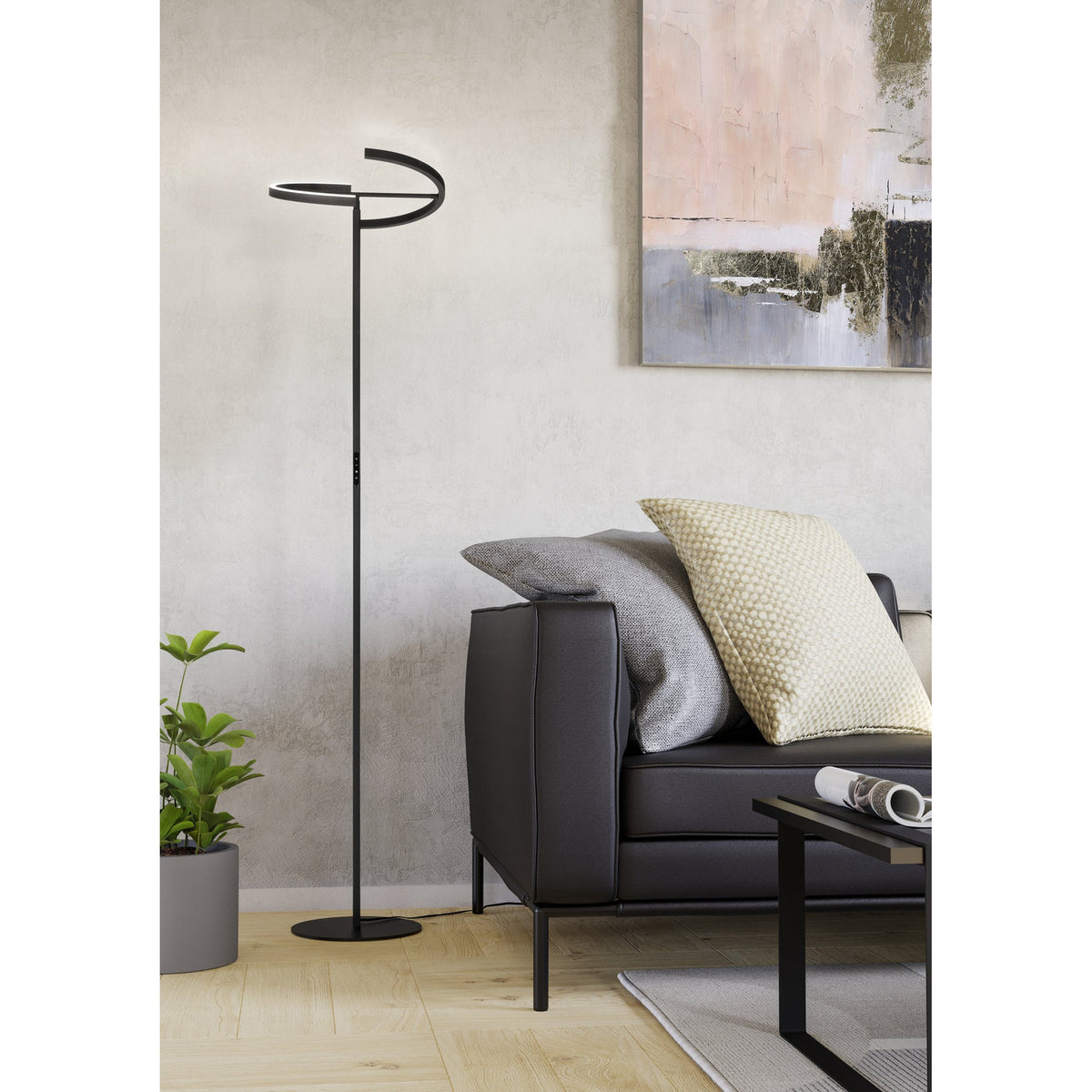 Castelpoto LED floor lamp in black steel with an angled open-ring shade on a slim stem and round base, shown beside a black sofa in a living room.