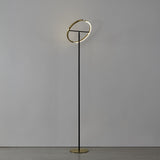 Castelpoto LED floor lamp with slim black steel stem, round brushed brass base and split ring head emitting warm white light, shown against a plain light grey background.