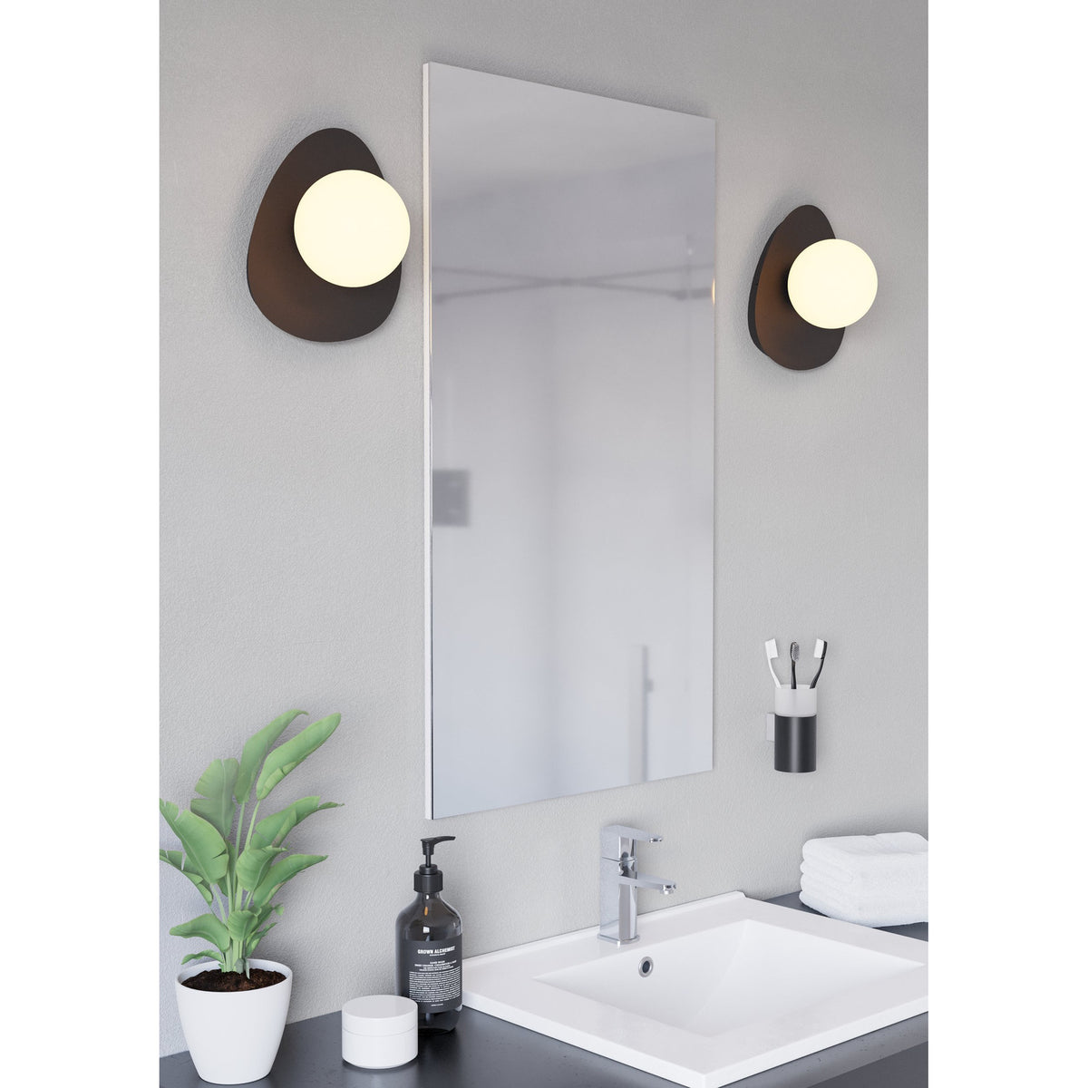 Castrovido Bathroom Wall Light in black steel with a pebble-shaped backplate and off-centre opal glass globe, shown flanking a mirror above a bathroom sink.