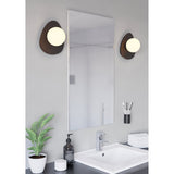 Castrovido Bathroom Wall Light in black steel with a pebble-shaped backplate and off-centre opal glass globe, shown flanking a mirror above a bathroom sink.