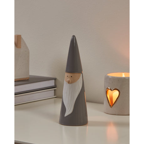 Catacol ceramic Santa ornament, a slim grey cone figure with pointed hat and textured white beard, displayed on a shelf beside a heart-cutout candle holder and stacked books.