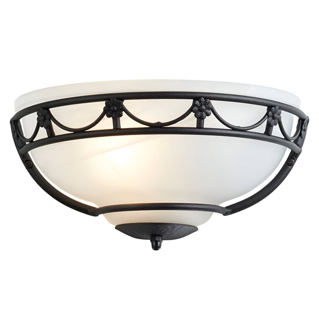 The Carisbrooke Wall Uplighter - Black features a gothic-inspired design with a white, alabaster-style glass shade and a black metal base adorned with decorative floral and curved designs. It emits a soft, warm light, adding an air of vintage sophistication to any space.