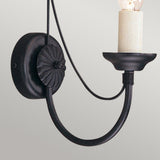 Introducing the Carisbrooke Wall Light - Black; a vintage-style wall sconce with a black metal frame, showcasing a decorative round base and a gracefully curved arm. Its candelabra-style design and candle-shaped bulb bring a classic touch against any neutral backdrop, enhancing your space with an elegant, vintage ambiance.