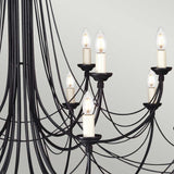Close-up of the Carisbrooke 18 Light Chandelier in black, featuring elegant candelabra-style arms with candle-shaped light bulbs. The curved design forms a sophisticated and intricate pattern, reminiscent of a Gothic-inspired chandelier, set against a neutral background.