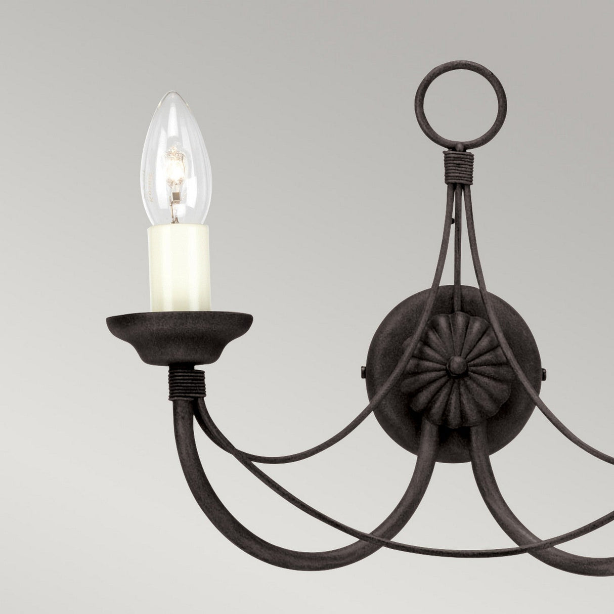 The Carisbrooke 2 Light Wall Light - Black exudes vintage charm with its black wrought iron design. This Gothic-inspired lighting piece features elegant curved arms and a round decorative backplate, beautifully enhanced by two candle-shaped light bulbs against a neutral gray background.