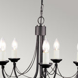 A close-up of the Carisbrooke 5 Light Chandelier - Black, showcasing its elegant candelabra-style arms adorned with several white candle-shaped bulbs, suspended from a chain against a light gray background. This chandelier features a classic, minimalist design with a subtle vintage appeal.