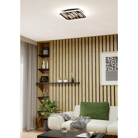 Cembrano LED flush ceiling light in black and natural wood-tone slats, shown on a living room ceiling above a wood-slat feature wall with shelving and a cream sofa.
