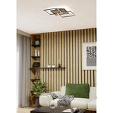 Cembrano 53cm square LED flush ceiling light with overlapping black frames and white edge diffusers, mounted above a wood-slat wall panel in a living room.