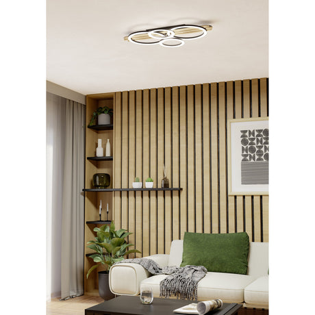 Cembrano LED Flush Ceiling Light 73cm in black & natural, with four overlapping ring shades on a wood and black felt slatted bar, shown mounted above a living room seating area.