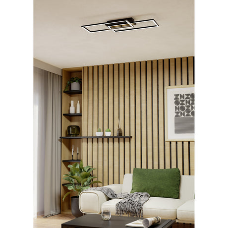 Cembrano LED flush ceiling light, 76cm, with two offset overlapping black rectangular frames and natural wood slat base, mounted in a living room with wood-slatted wall.