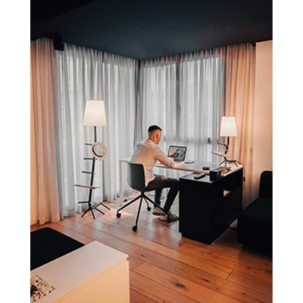 Centipede table lamp with black branching metal base and white conical shade beside a desk where a man works on a laptop.