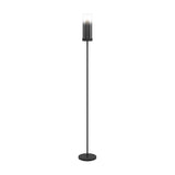 Cesarne Floor Lamp in black steel with a slim column and round base, topped by a cylindrical smoked glass shade fading to clear, single E27 fitting, on a plain white background.