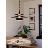 Cesmine Pendant Light in black steel with layered disc and dome shades revealing a copper-toned underside, hanging above a dining table in a styled living space.