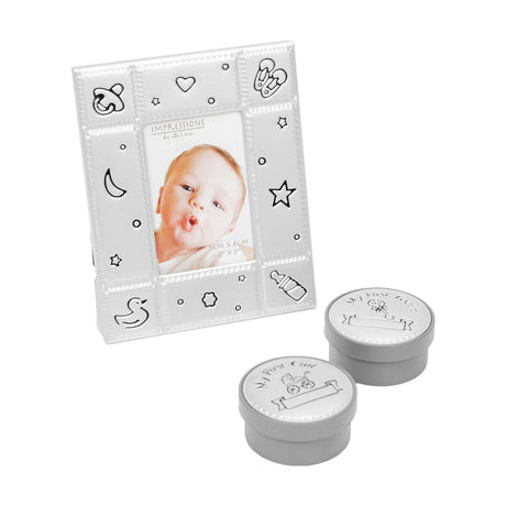 Silver-finish metal photo frame with embossed baby motifs, paired with round keepsake boxes labeled My First Curl and My First Tooth on grey bases, white background.