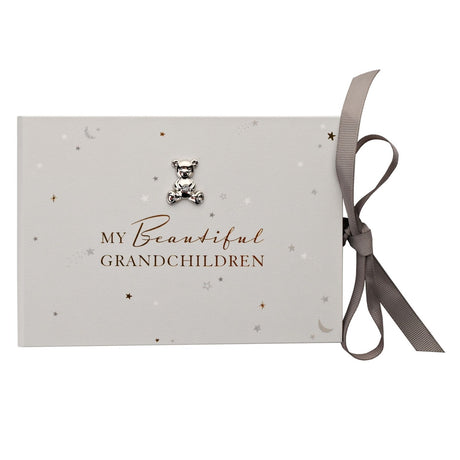 White photo album with star and moon print, "My Beautiful Grandchildren" foiled text, silver teddy bear charm, and grey ribbon tie on a plain background.