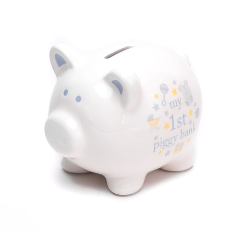 White ceramic piggy money box with blue ear and eye details, coin slot on back, and "my 1st piggy bank" text with star and rattle motifs on a plain background.