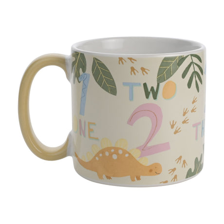 Dinosaur Numbers stoneware mug in beige with pastel number prints, an orange stegosaurus design, leaf motifs, and a pale yellow handle, shown on a plain white background.