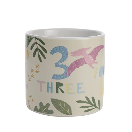 Dinosaur Numbers Stoneware Mug in beige with pink pterodactyl, number "3" and "THREE" lettering, leaf and footprint details, on a plain white background.