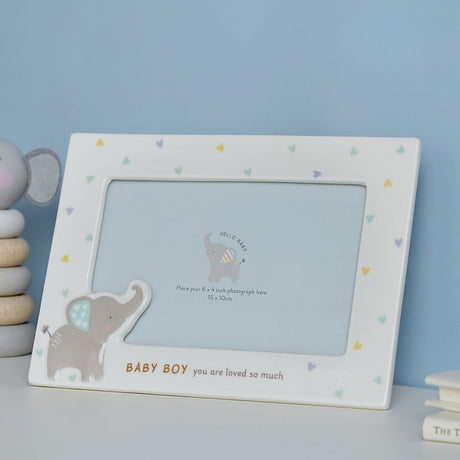 White ceramic rectangular photo frame for a baby boy, with a grey elephant motif, pastel hearts, and "BABY BOY you are loved so much" text, shown on a nursery shelf.