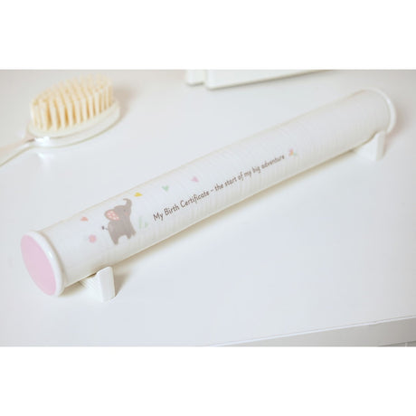 White ceramic birth certificate keepsake box with a pink end cap, decorated with a grey elephant, hearts and florals, shown on a white surface beside a hairbrush.