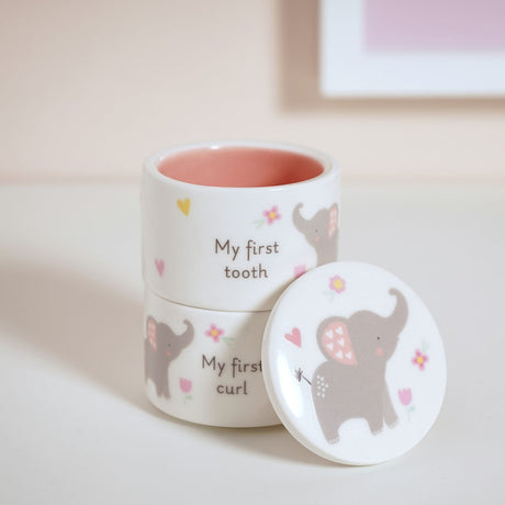 White ceramic keepsake box set with "My first tooth" and "My first curl" pots, pink interiors, elephant and floral design, one lid resting against the stack.