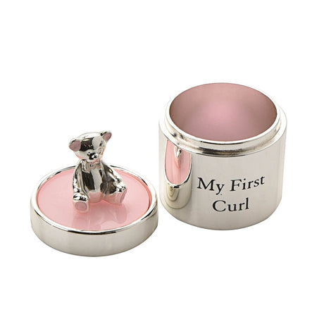Silverplated round keepsake box labelled "My First Curl" with pink enamel lid and interior, topped by a small silver teddy bear with pink ears and feet, on a white background.