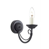 The Chartwell 1 Light Wall Light - Black boasts a timeless candelabra style with a curving arm and an exposed bulb that mimics the look of a candle. The round base is beautifully detailed with a decorative rosette pattern, enhancing its classic black finish.