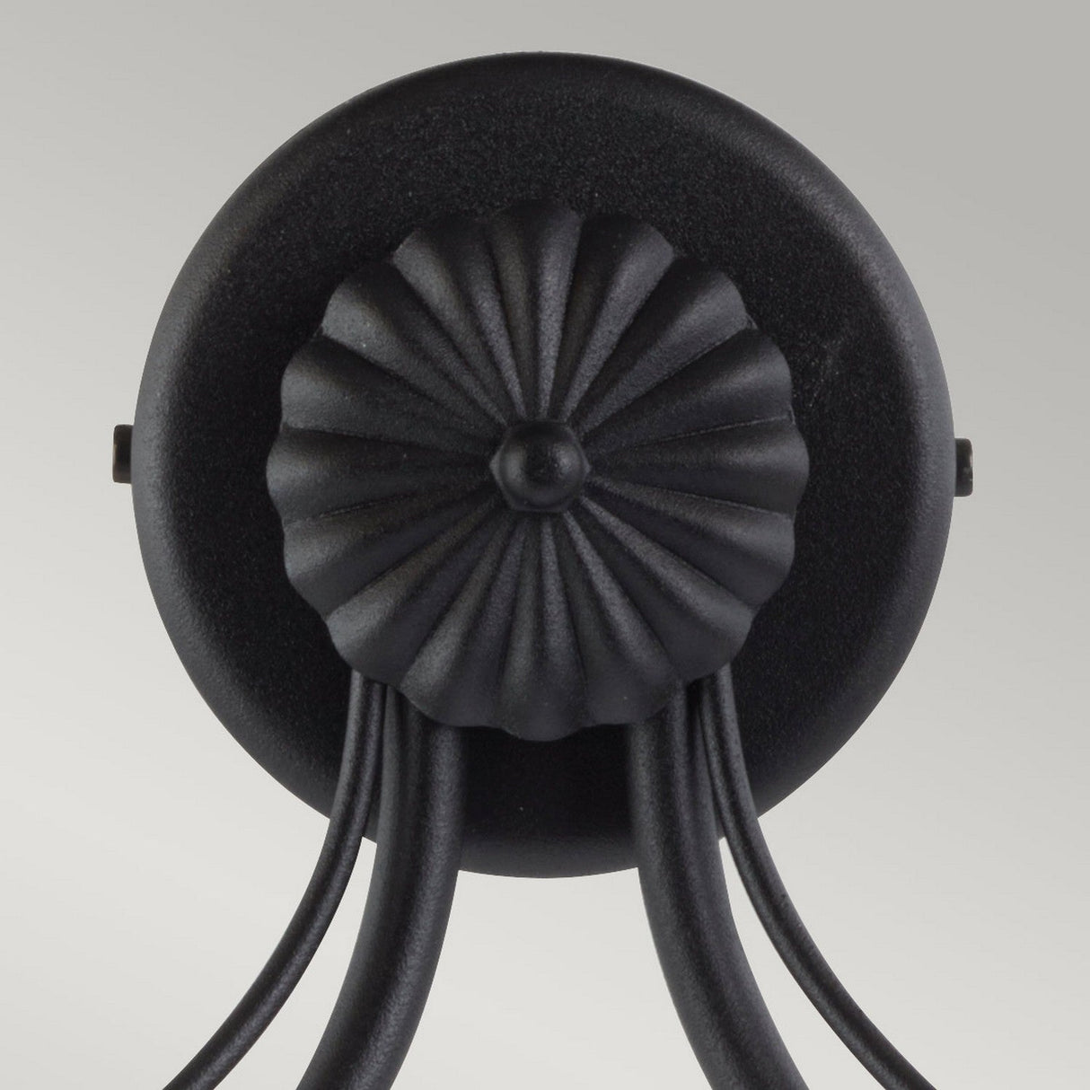 Close-up of a decorative black ceiling light fixture, exuding traditional charm with its circular base and fluted pattern. Multiple curved arms extend downward, reminiscent of the Chartwell 2 Light Wall Light - Black. The background is a soft gray, adding a modern touch.