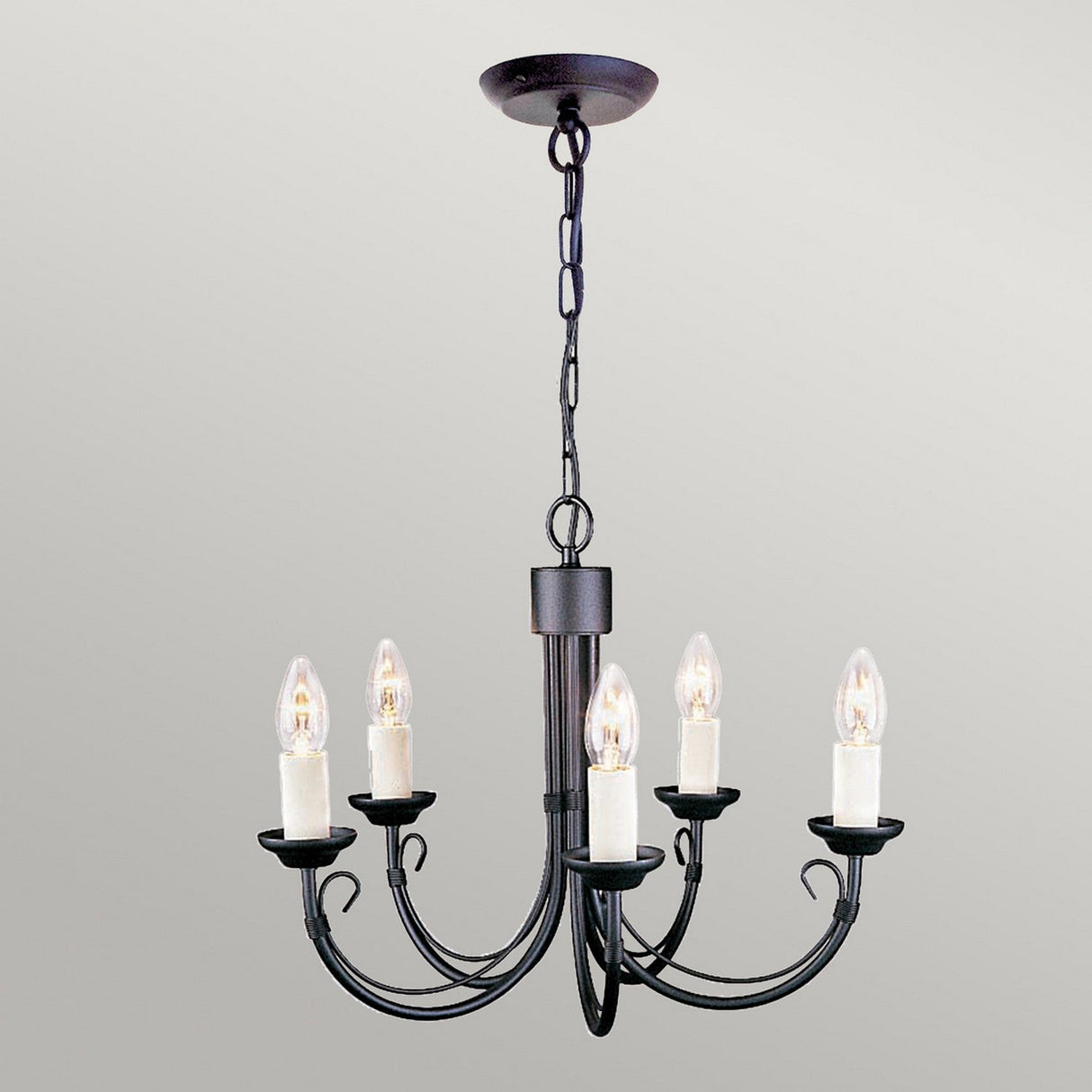 The Chartwell 5 Light Chandelier - Black, featuring a classic design with five candle-shaped light bulbs, is elegantly suspended from the ceiling by a chain, providing timeless lighting solutions against a simple, light-colored background.