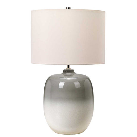 The Chalk Farm Table Lamp in Light Grey/Chalk White showcases a modern design with its glossy, gradient gray ceramic base and large cylindrical faux silk shade. A polished nickel finial adds an elegant touch, making this lamp ideal for sleek and minimalist contemporary interiors.