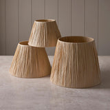 Endon Chartshaw tapered lamp shades in natural raffia, shown in three sizes grouped on a pale stone surface against a light grey panelled background.