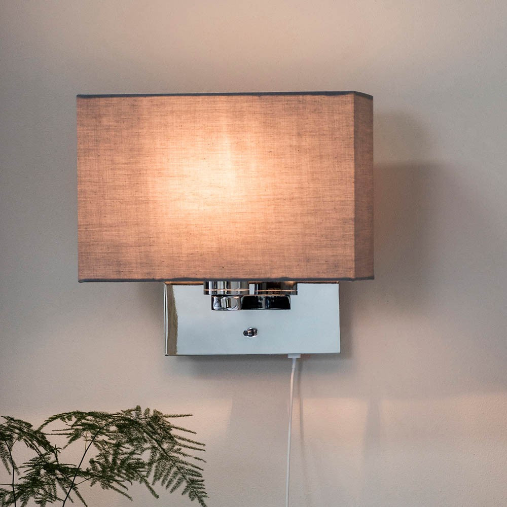 Chartstead rectangular tapered lamp shade in grey fabric, shown illuminated on a chrome wall light fixture with pull-cord switch.
