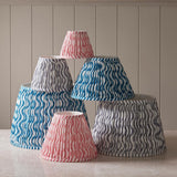 Endon Chartwood tapered lamp shades in marlin blue, pearl grey and coral pink, stacked in pleated faux linen with rippled prints and taped edges.