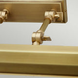 A close-up of the Chawton Large Picture Light - Aged Brass showcases its adjustable joints and rods, offering directional lighting against a light gray backdrop. This fixture effortlessly combines structural elegance with decorative charm.