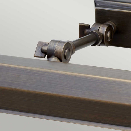 Close-up of a dark bronze-colored metal hinge with a rod connecting two segments, featuring a slightly textured surface. This hinge, reminiscent of the Chawton Medium Picture Light - Dark Bronze design, is part of a larger structure, set against a neutral background ideal for illuminating artwork.