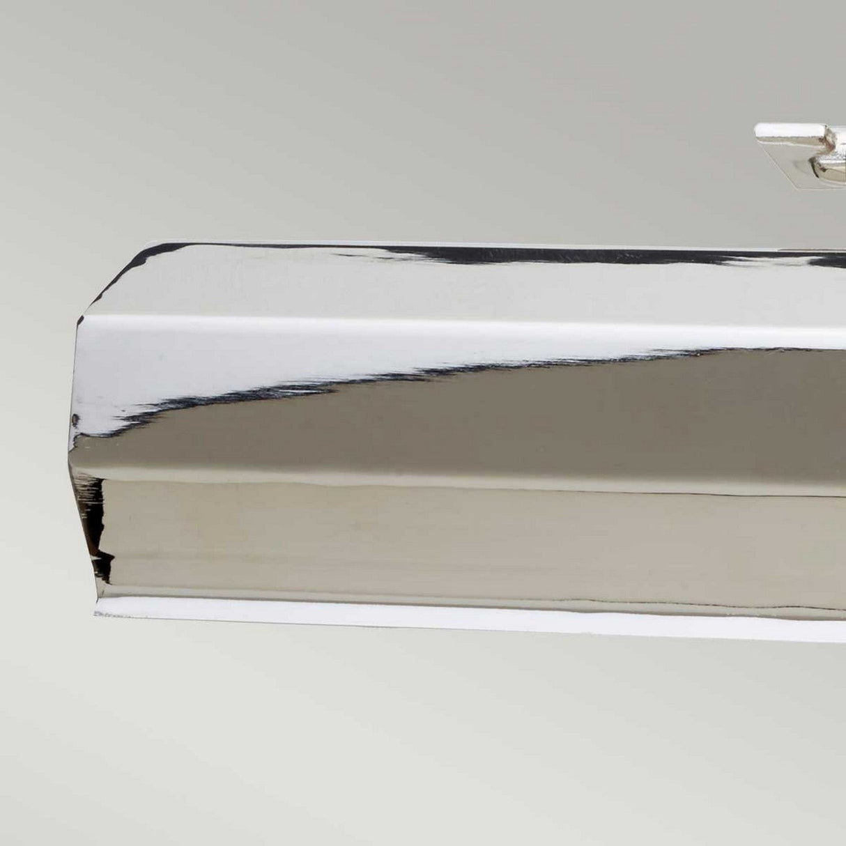 A close-up view of a metallic rectangular object with a shiny, reflective surface, mounted against a light gray background. The object's clean lines and polished nickel finish suggest it could be the Chawton Medium Picture Light - Polished Nickel, complete with adjustable knuckle joints for precise positioning.