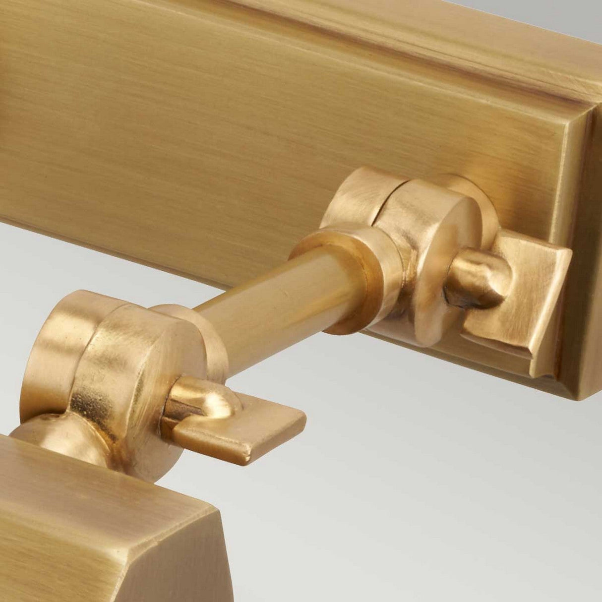 A close-up of the Chawton Small Picture Light in aged brass showcases its contemporary elegance with a joint and pivot mechanism. This design offers a sleek finish, incorporating both rectangular and cylindrical elements for stylish directional lighting.