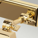 A detailed view of the Chawton Small Picture Light in polished brass reveals its shiny, reflective surface. The light is mounted to a rectangular fixture with a polished finish, highlighting its sophisticated design. The backdrop is a simple, light gray.