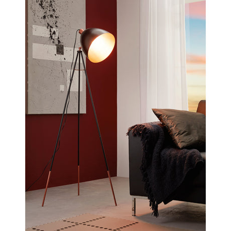 Chester Floor Lamp in black and copper, a tripod steel floor lamp with slanted legs and a tilted spotlight-style shade, shown lit beside a sofa in a living room.