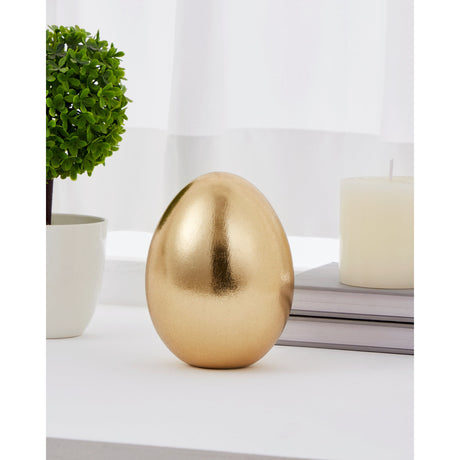 Chilandy ceramic decorative egg in gold with a flecked, light-catching texture, standing upright on a shelf beside a candle and a small potted plant.