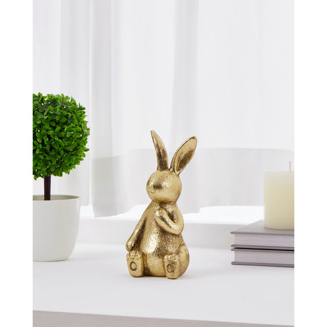 Chilandy Rabbit Ornament in gold resin with textured finish, seated with one paw raised and ears upright, displayed on a windowsill beside a plant and candle.