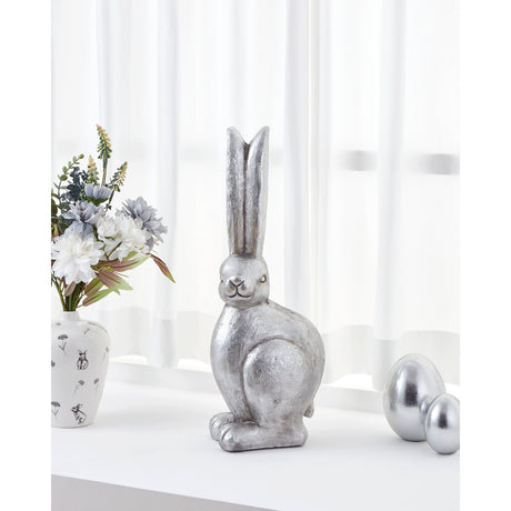 Chilandy stone rabbit ornament in nickel finish with tall upright ears and a textured silver body, displayed on a windowsill beside silver egg ornaments and a floral vase.