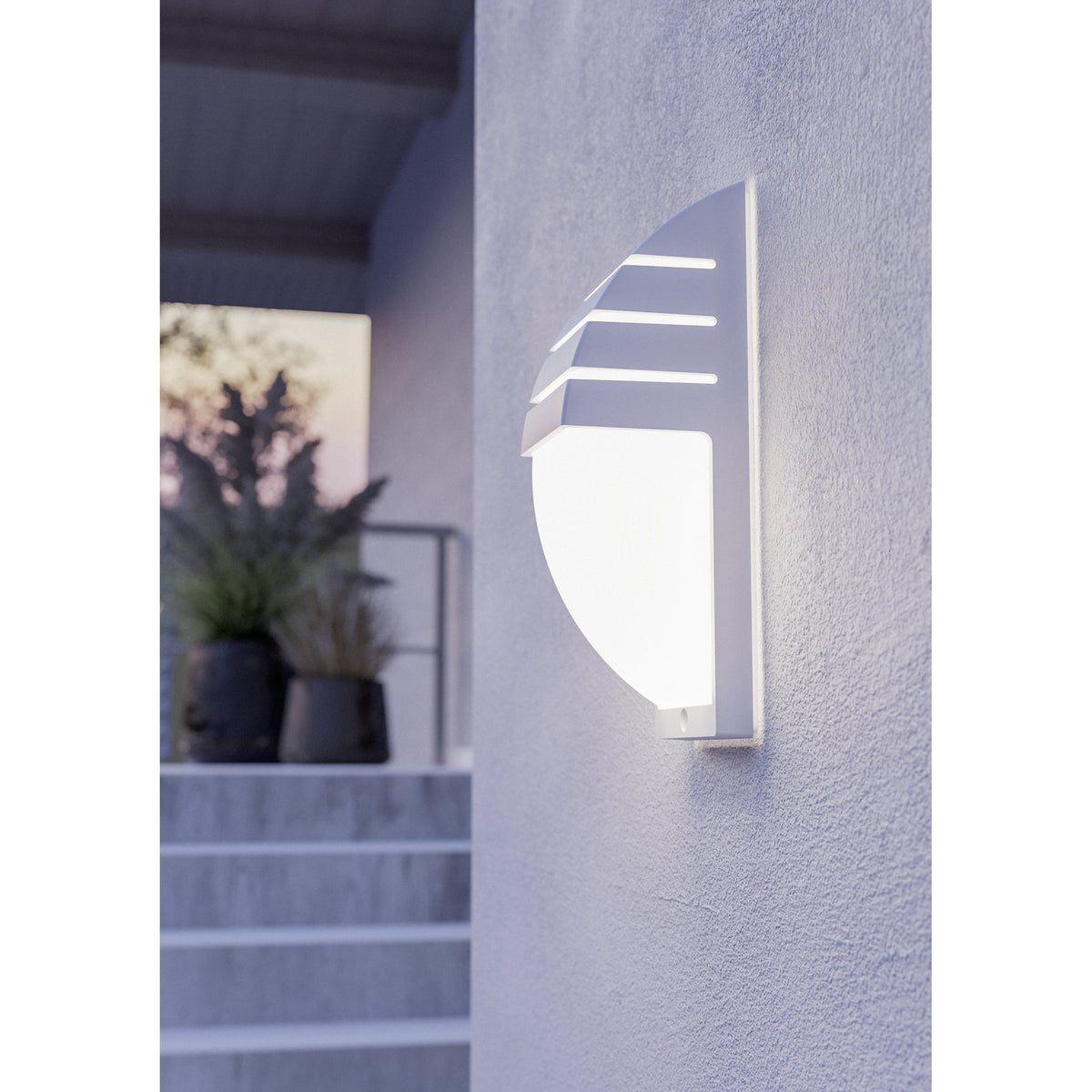 Cimoneri-E outdoor wall light in white plastic, mounted on an exterior wall, with a curved louvred hood over an illuminated opal diffuser, shown near a doorway with steps and potted plants.
